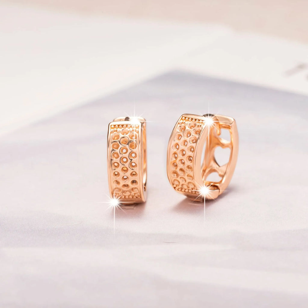 A pair of circular rose gold tone earrings featuring a hollowed-out heart shape design on a white background.