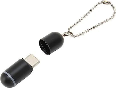 Small black capsule infrared emitter remote control for smartphones next to a phone.