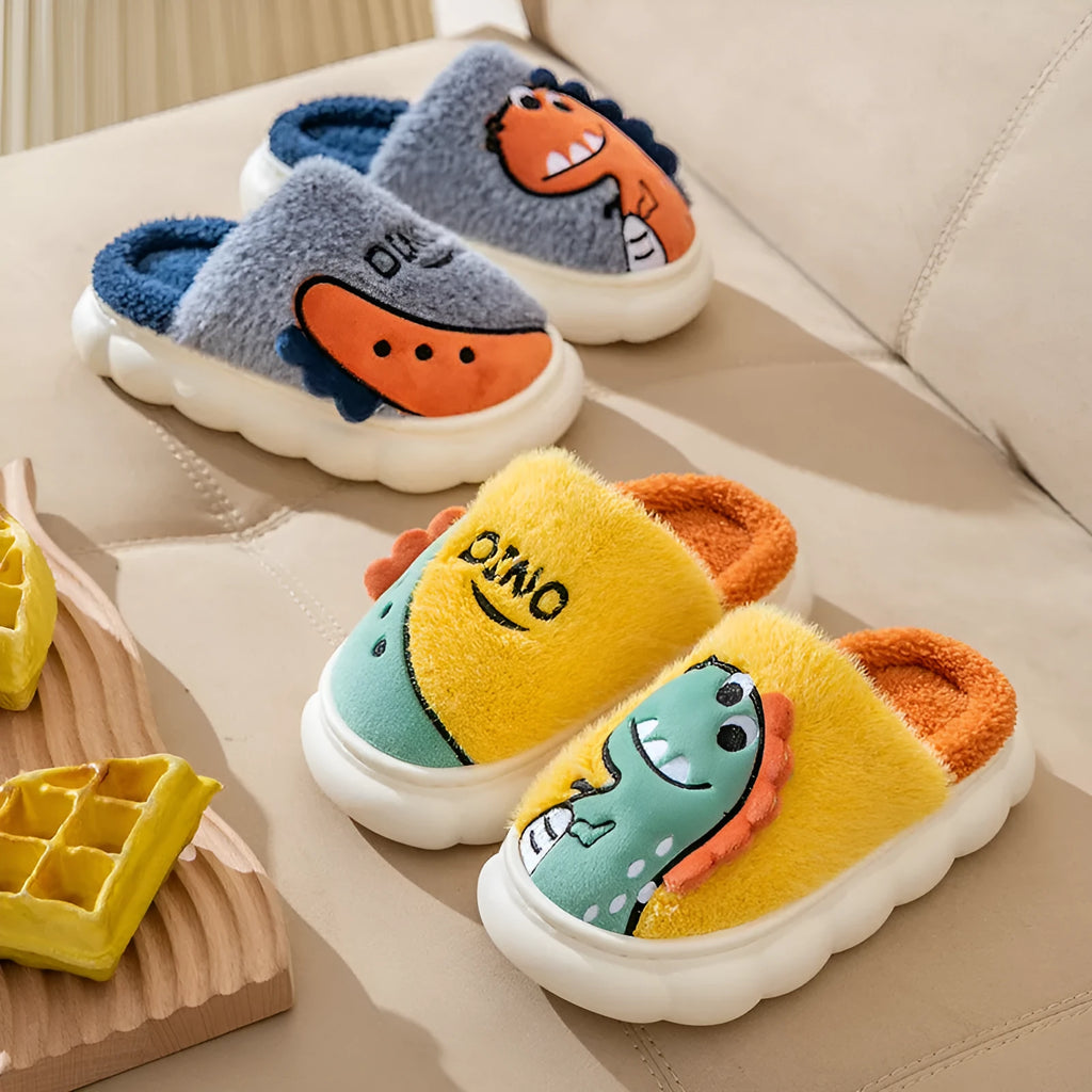 A pair of grey dinosaur-print plush slippers on a wooden floor, showing the soft cotton upper and thick textured sole.