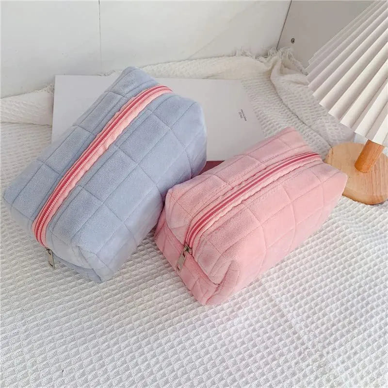 Three plush makeup bags in pink, white, and blue with zippers, laid flat showing front
