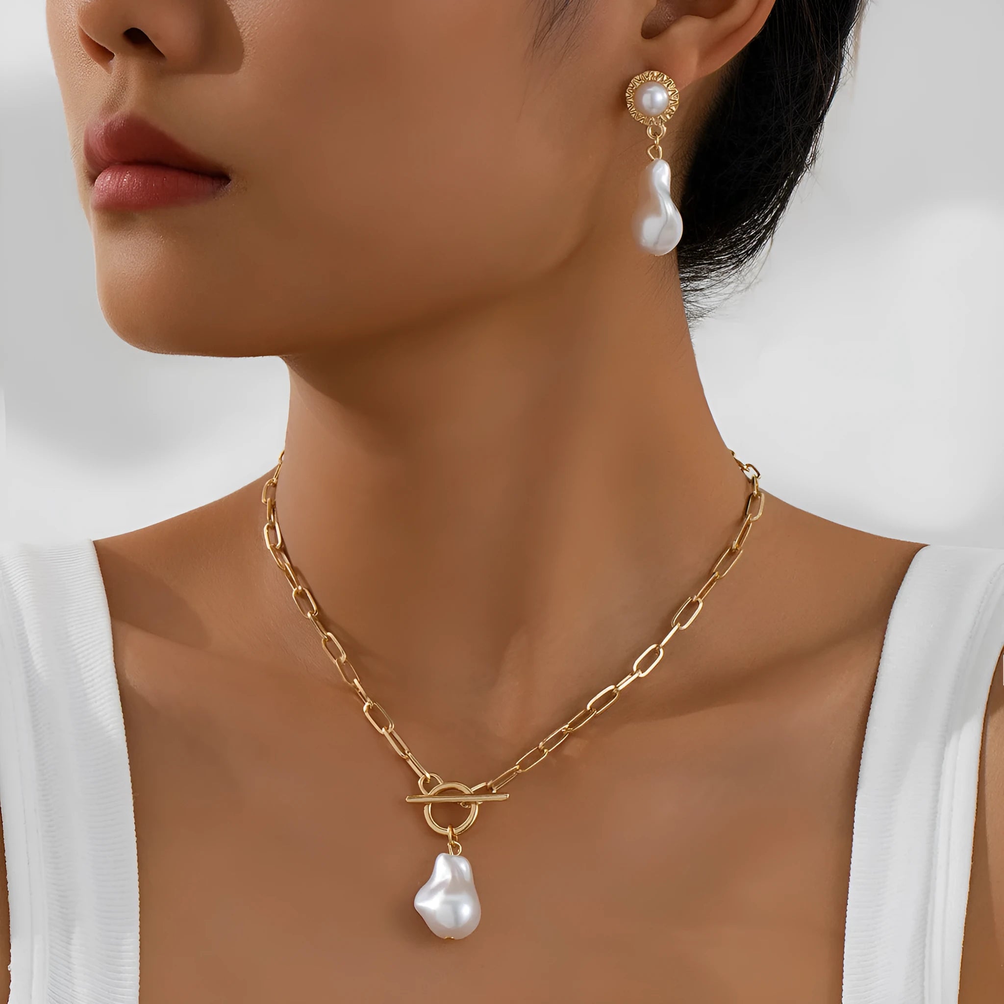 Gold-toned baroque pearl pendant necklace and matching stud earrings set on a dark background.