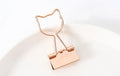 Small gold metal office clip with a long tail, shown in flamingo, love, cloud, cat, cactus, and bow shapes.