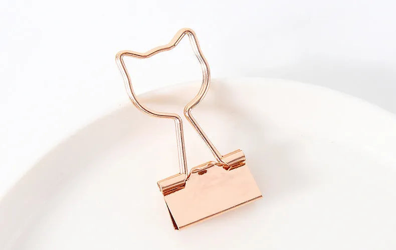 Small gold metal office clip with a long tail, shown in flamingo, love, cloud, cat, cactus, and bow shapes.