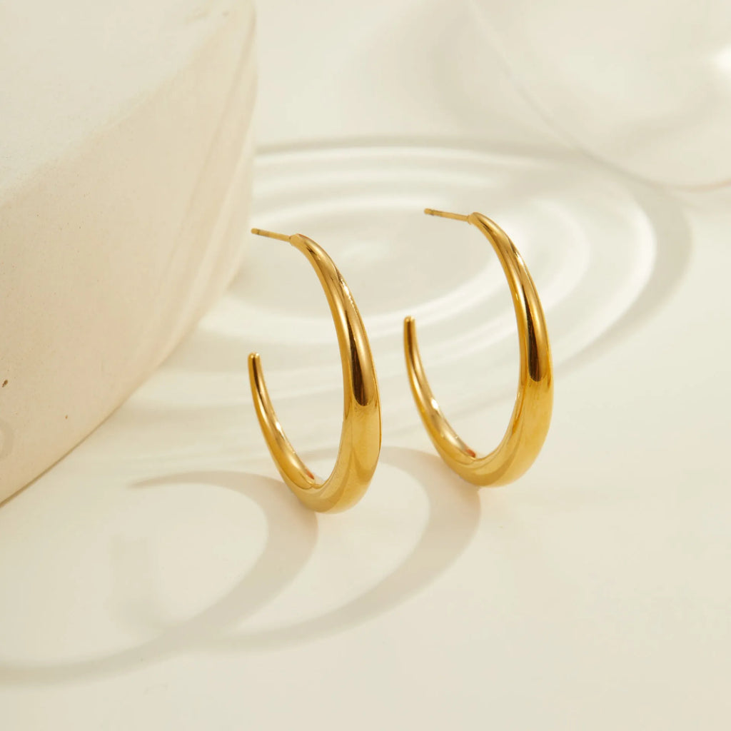 A pair of round titanium steel hoop earrings with an 18K gold plated finish, shown in large and small size options.