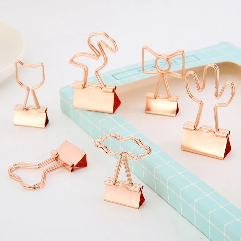 Small gold metal office clip with a long tail, shown in flamingo, love, cloud, cat, cactus, and bow shapes.