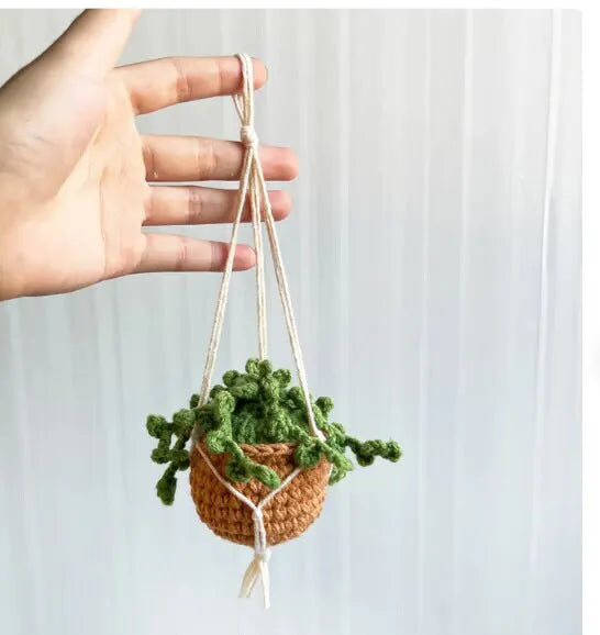 Green and white crocheted wool car plant decoration with a white hanging rope.