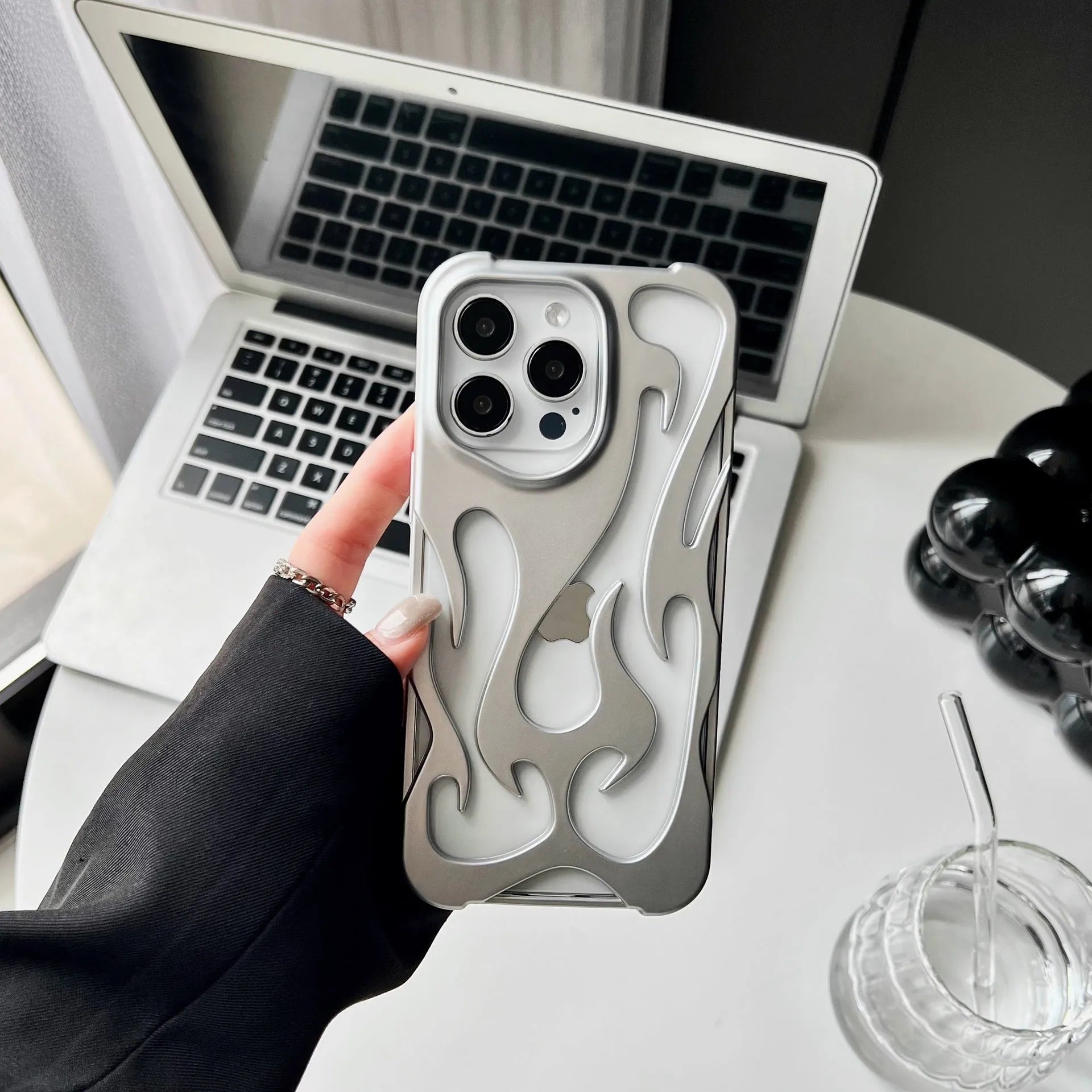 Electroplated hollow flame pattern phone case for iPhone on a table, showing silver metallic finish and cut-out design.