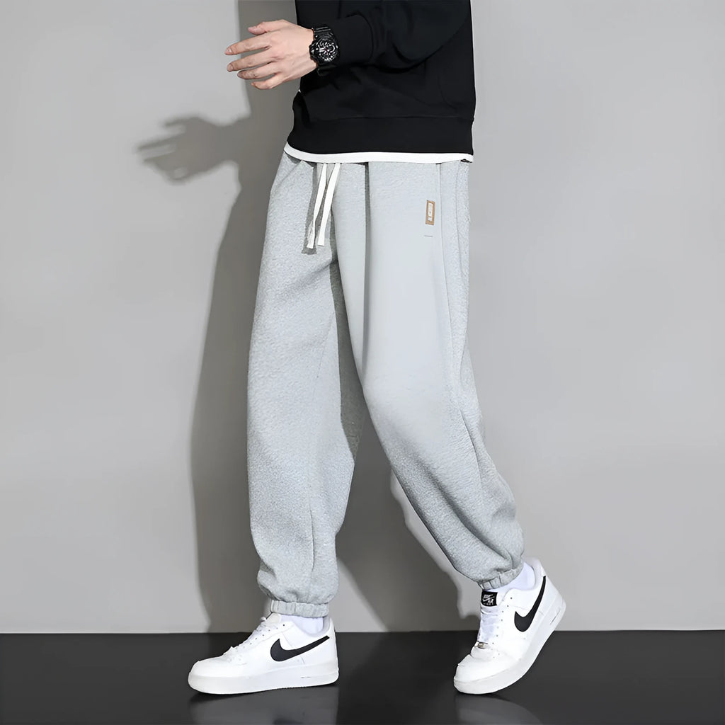 Men's loose grey cotton blend sports trousers with a drawstring waist on a hanger.