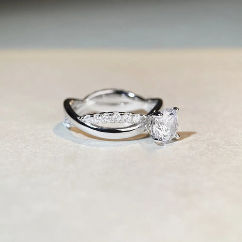 A silver ring with a 1 karat moissanite stone in a four-claw setting on a twisted geometric band.