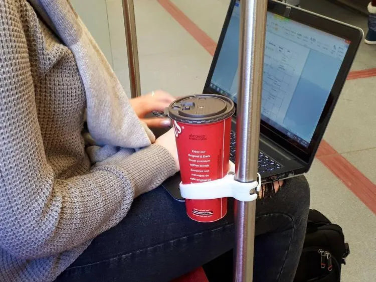 Portable transportation cup holder in red, attached to a bus handrail, holding a coffee cup