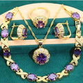 Gold jewellery set with sparkling blue cubic zirconia stones, showing necklace, earrings, ring, and bracelet on a dark background.