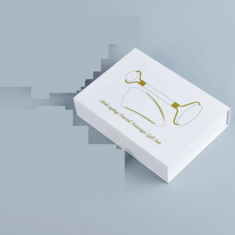 White jade facial roller and gua sha scraping board set on a table.