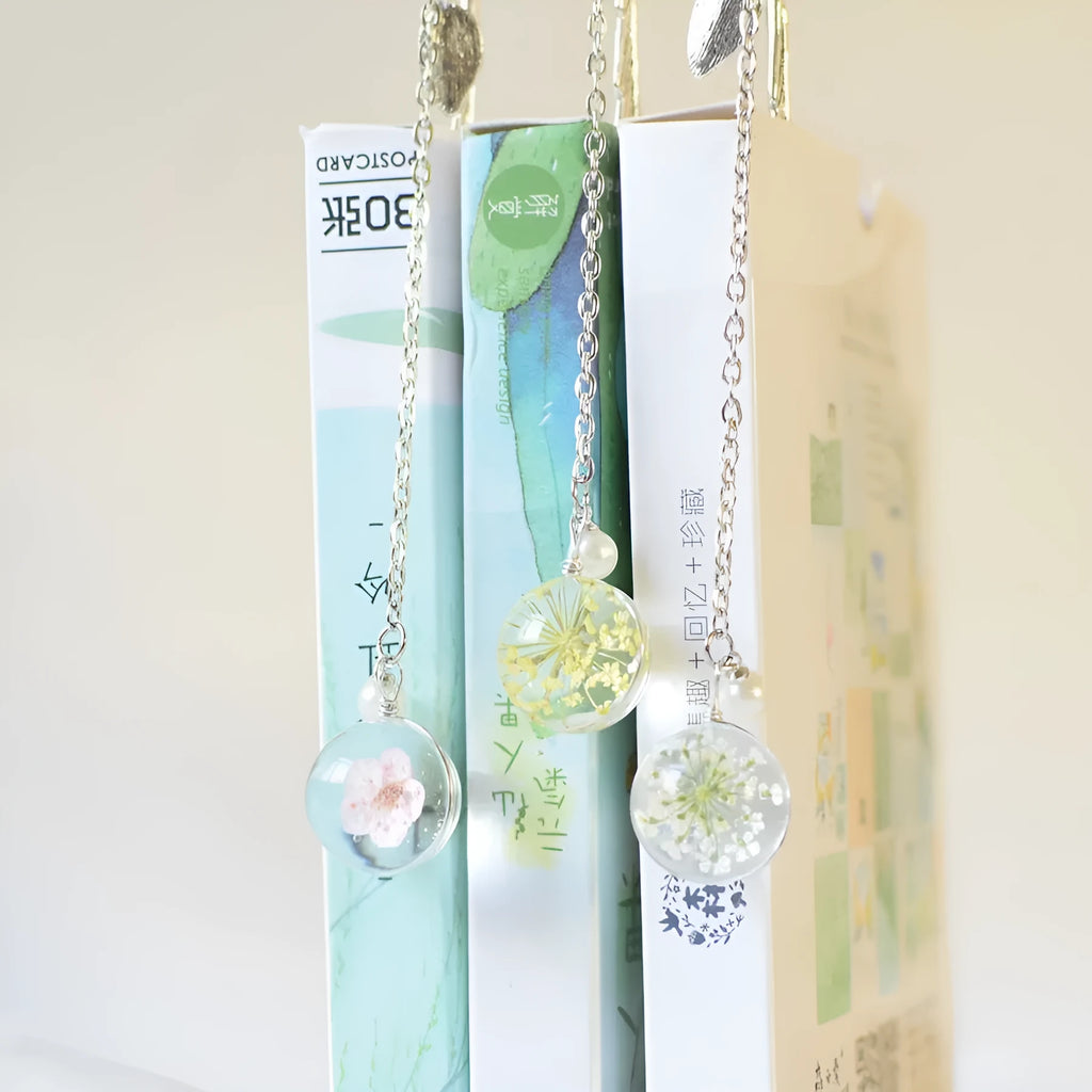 Close-up of a metal alloy bookmark with a preserved pink dried flower inside, measuring 12cm long, on an open book.