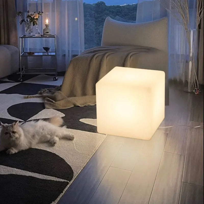 A modern square white LED cube light stool in a garden setting, showing its size options.