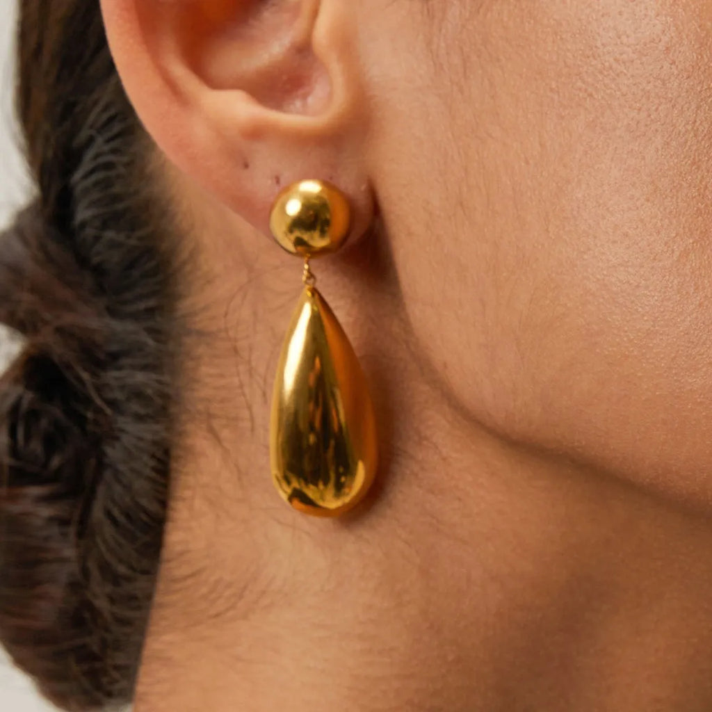 A pair of gold-coloured geometric hemisphere earrings with a hanging water droplet pendant.