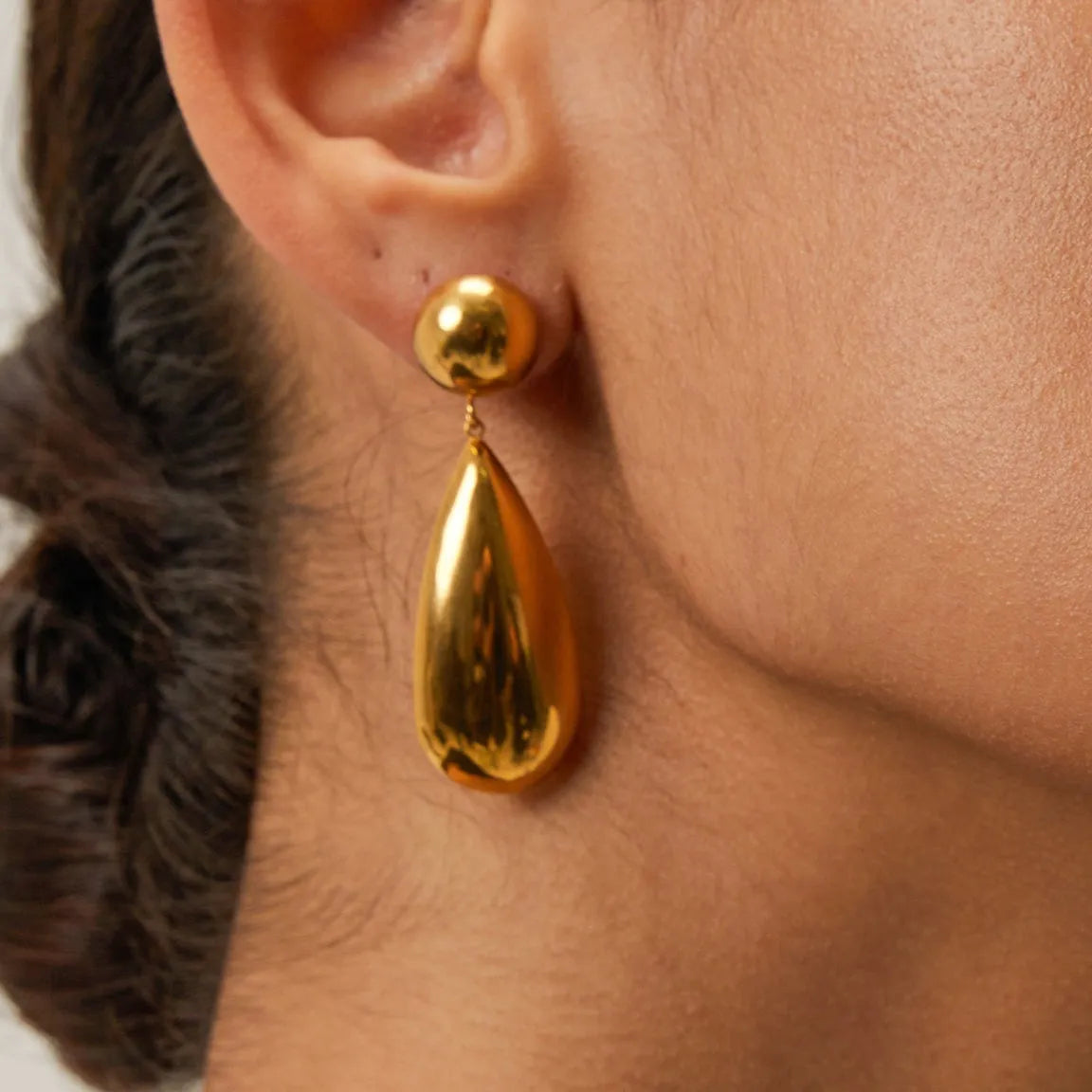 A pair of gold-coloured geometric hemisphere earrings with a hanging water droplet pendant.