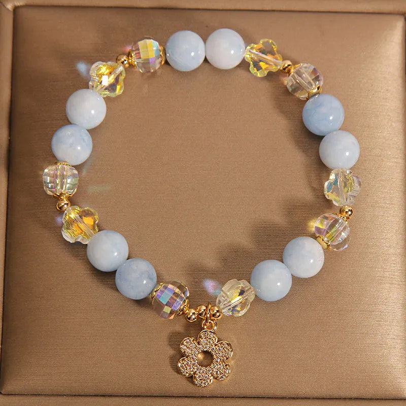 Women's aquamarine crystal bracelet with a four-leaf clover charm and pearl accent on wrist.