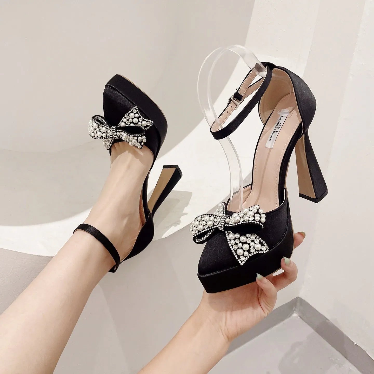 Women's black satin pointed-toe pump with a decorative bow and an adjustable loop strap over the instep.