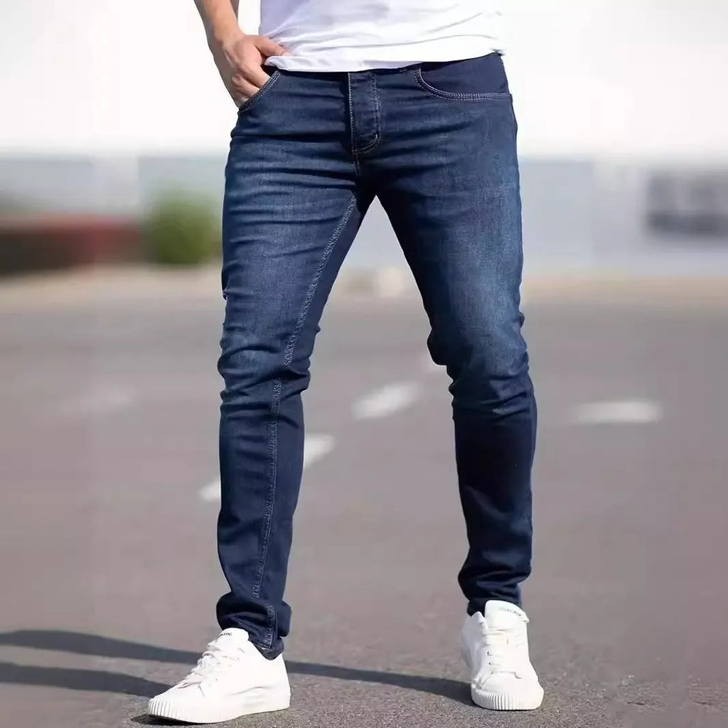 Men's dark blue slim-fit skinny jeans with a zip fly and mid-rise waist on a plain background.