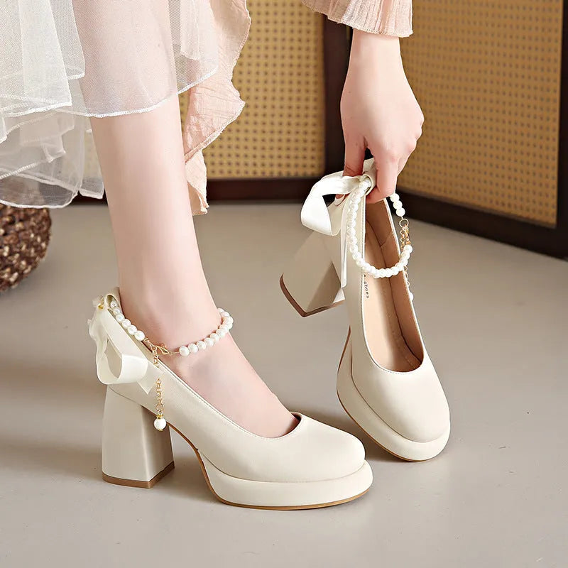 Beige women's Mary Jane shoes with chunky heel, round toe, and pearl- detail ankle strap on a white background.
