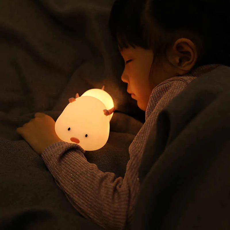 Pink silicone night light in the shape of a sleeping pig on a table.