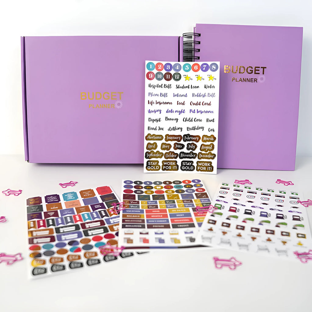 J12 purple coil-bound financial planning notebook with pen, stickers, and paper clips on a desk.