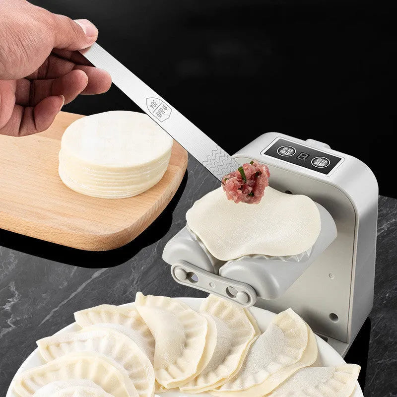White automatic electric dumpling maker machine with USB cable, brush, and spoon on a kitchen counter.