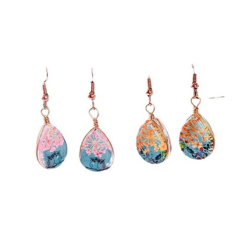Water drop-shaped glass eardrops earrings with owl motif in ginger yellow and pink coloured glaze on a light background