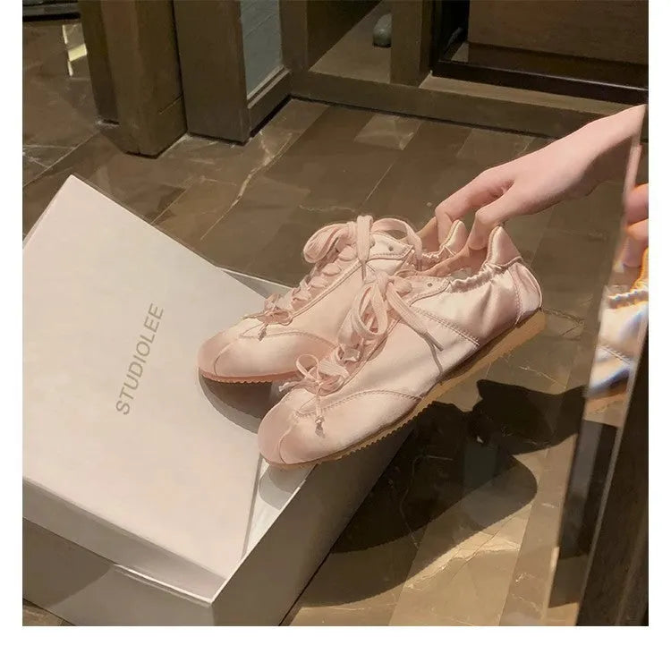 Women's champagne pink satin ballet flat shoes with a round toe and white front lace-up detail.
