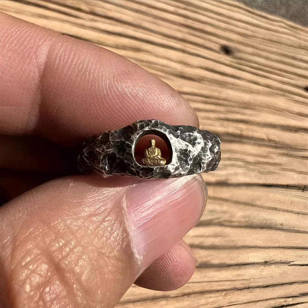 Close-up of a hand-forged copper ring with a rock texture and a carved Buddha design.