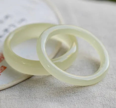 A polished natural jade round bar bracelet showing a winding silk texture on its surface.