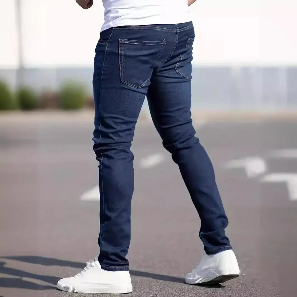 Men's dark blue slim-fit skinny jeans with a zip fly and mid-rise waist on a plain background.