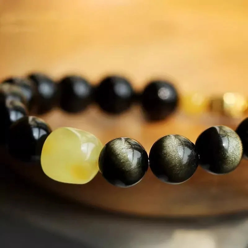 Golden obsidian bracelet with geometric beads and a detailed zodiac animal charm on a wrist.