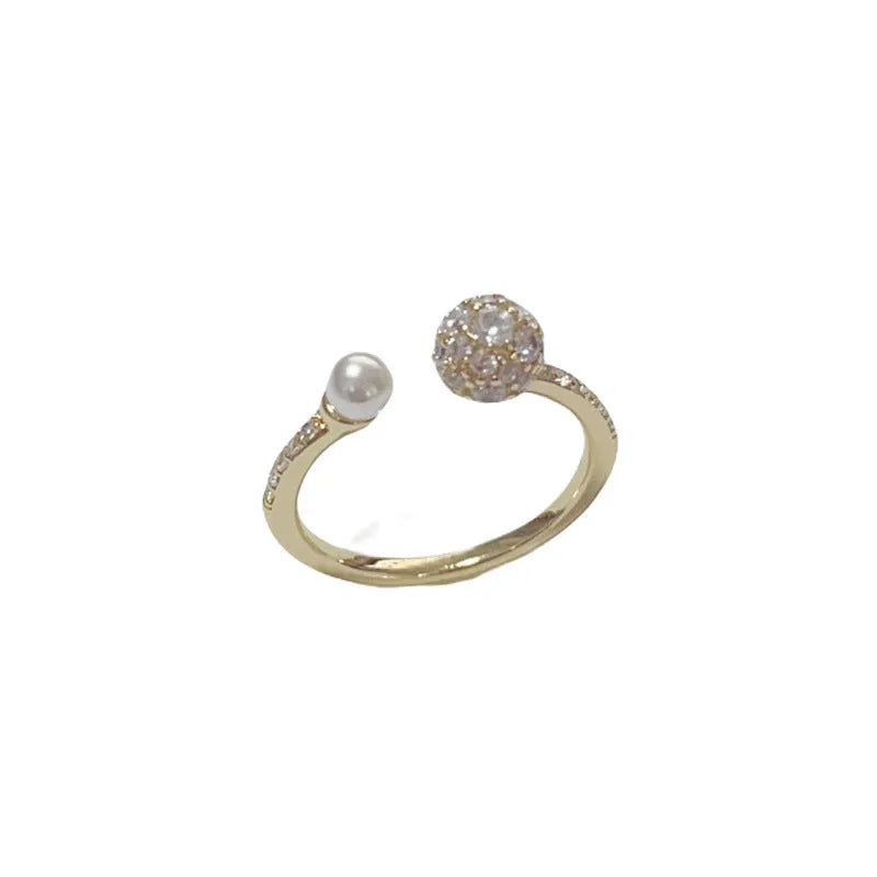 Open-end pearl ring with round zircon stone in gold or silver colour finish.