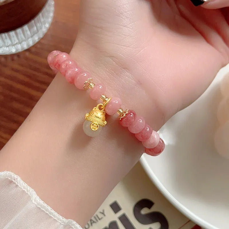 Women's strawberry quartz bracelet with lucky cat charm on grey background