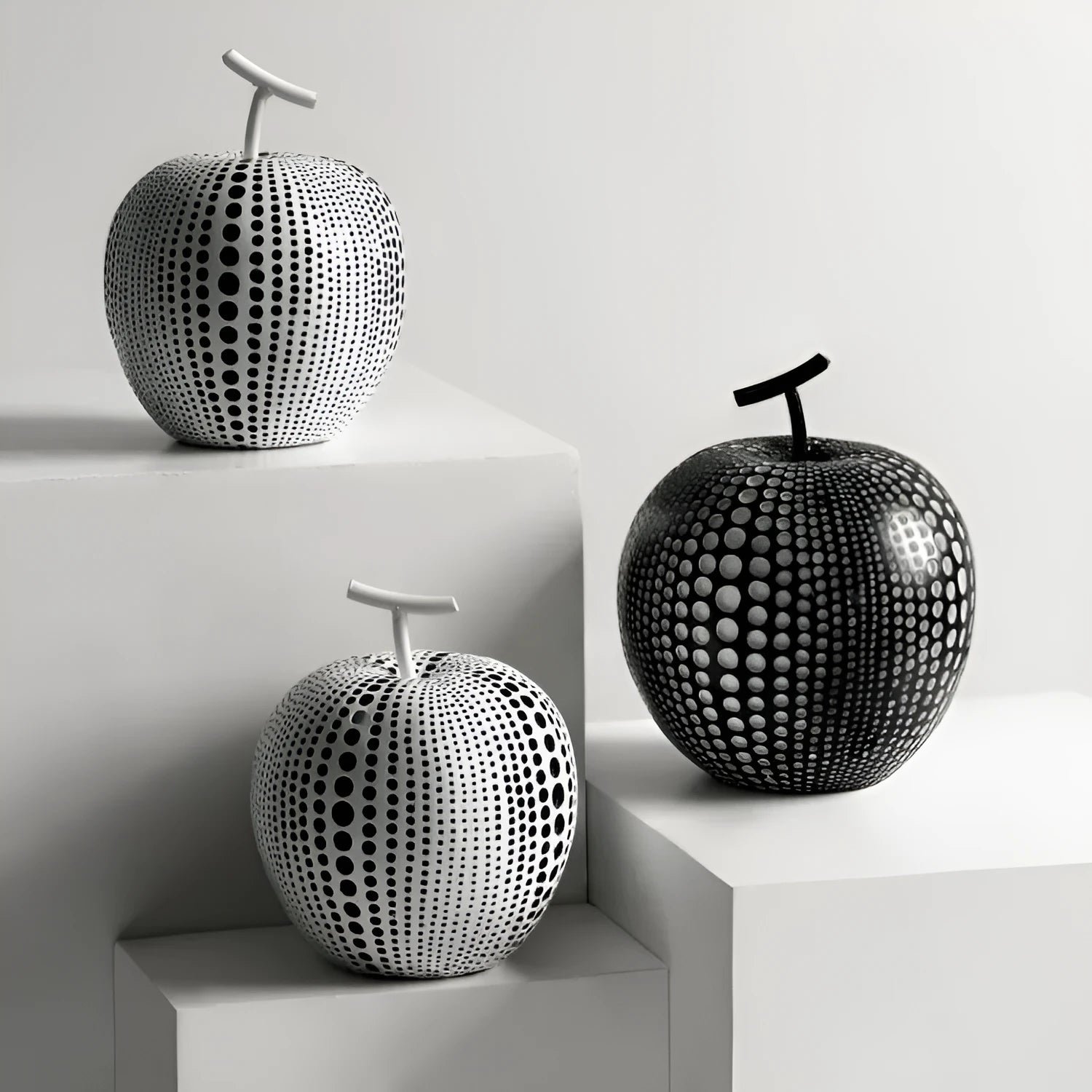 A tall black resin vase and a low white resin apple decoration on a wooden table.