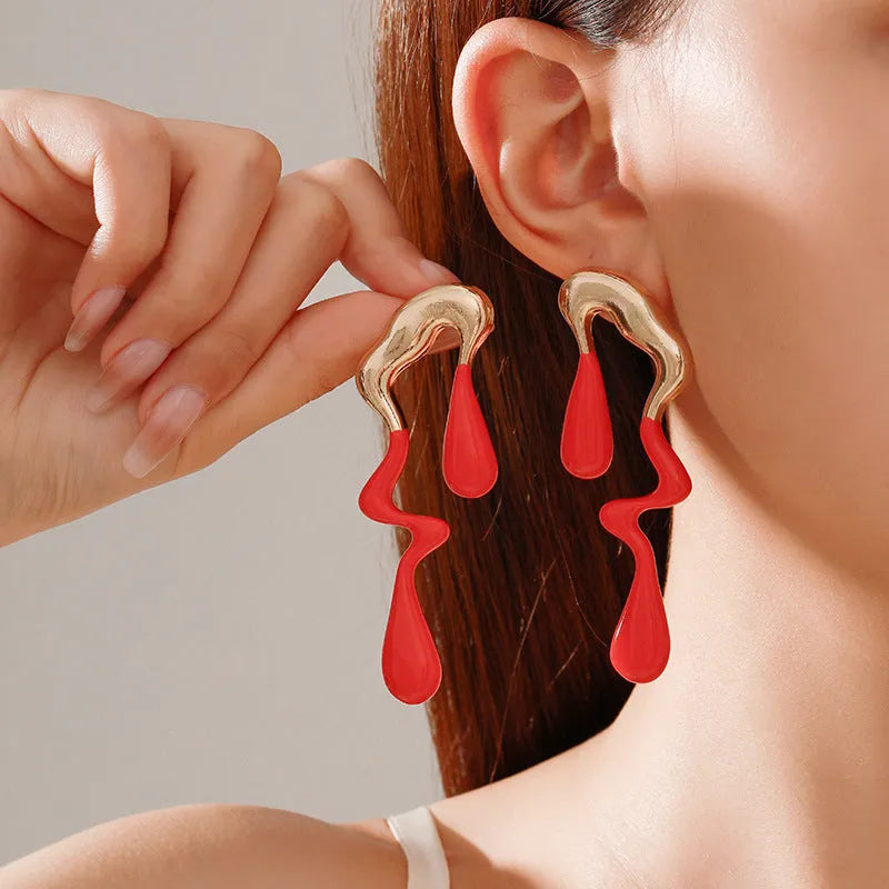 A pair of liquid irregular geometric water drop ear studs in gold finish on a neutral background