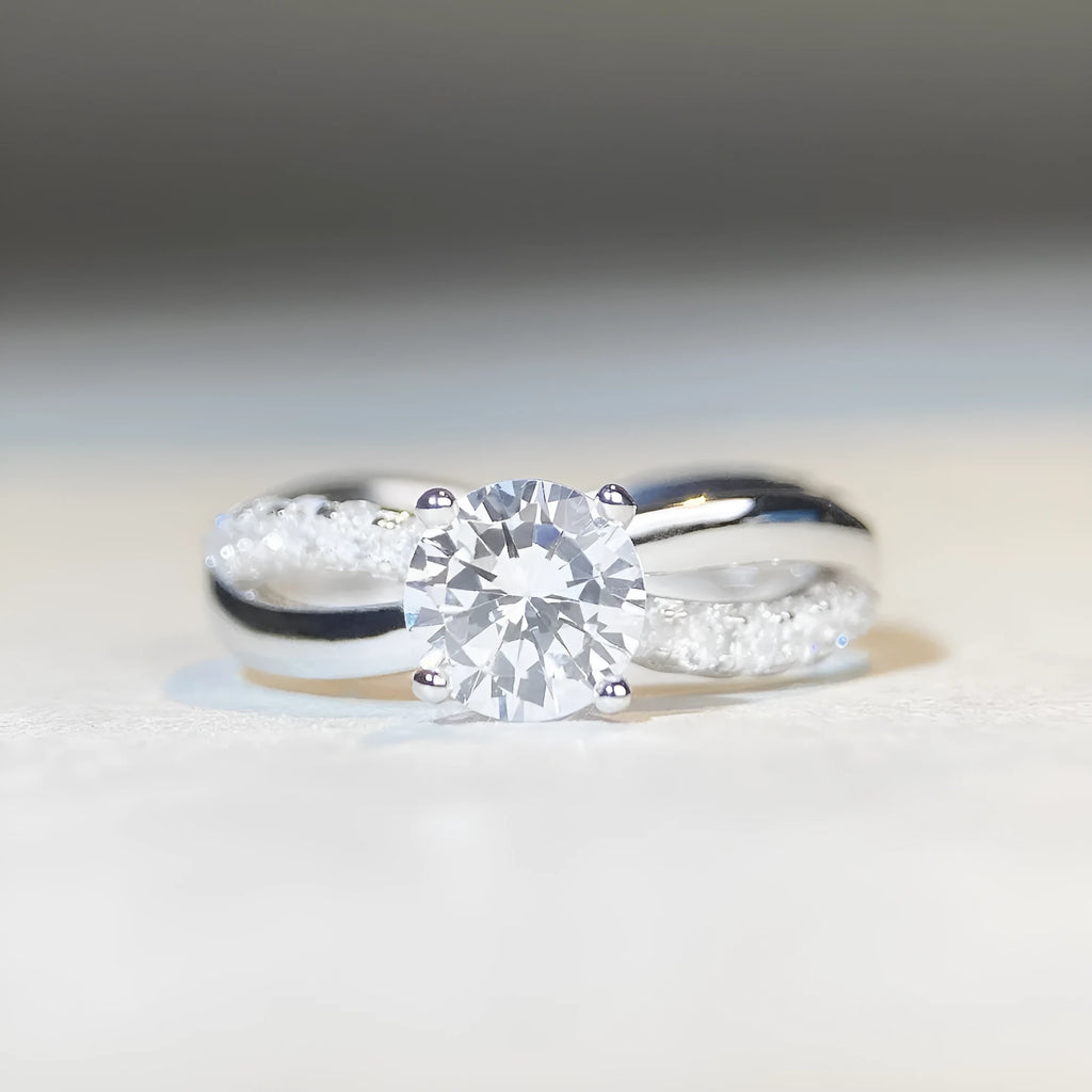 A silver ring with a 1 karat moissanite stone in a four-claw setting on a twisted geometric band.
