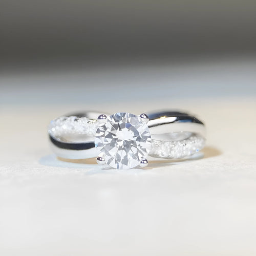 A silver ring with a 1 karat moissanite stone in a four-claw setting on a twisted geometric band.
