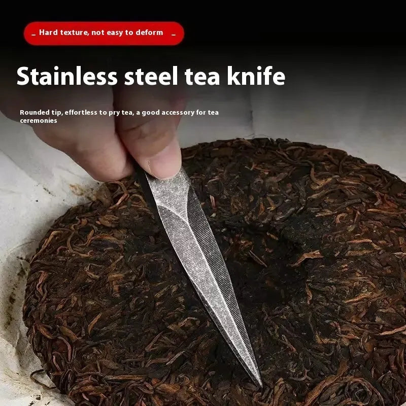 Black stainless steel hand pry tea knife on dark surface with tea leaves