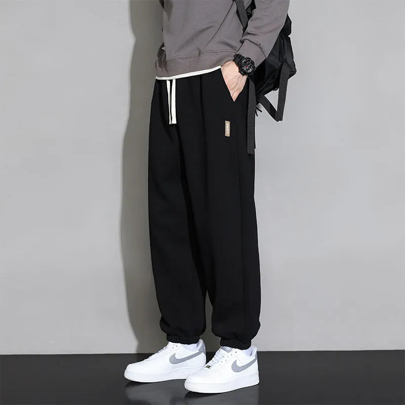 Men's loose grey cotton blend sports trousers with a drawstring waist on a hanger.