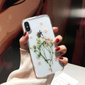 Clear TPU iPhone case showing real pink dried flowers encapsulated in epoxy resin on the back.