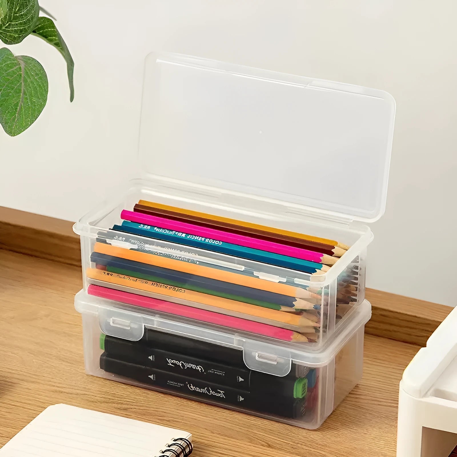 Clear transparent plastic storage box filled with coloured pencils and crayons with lid open.