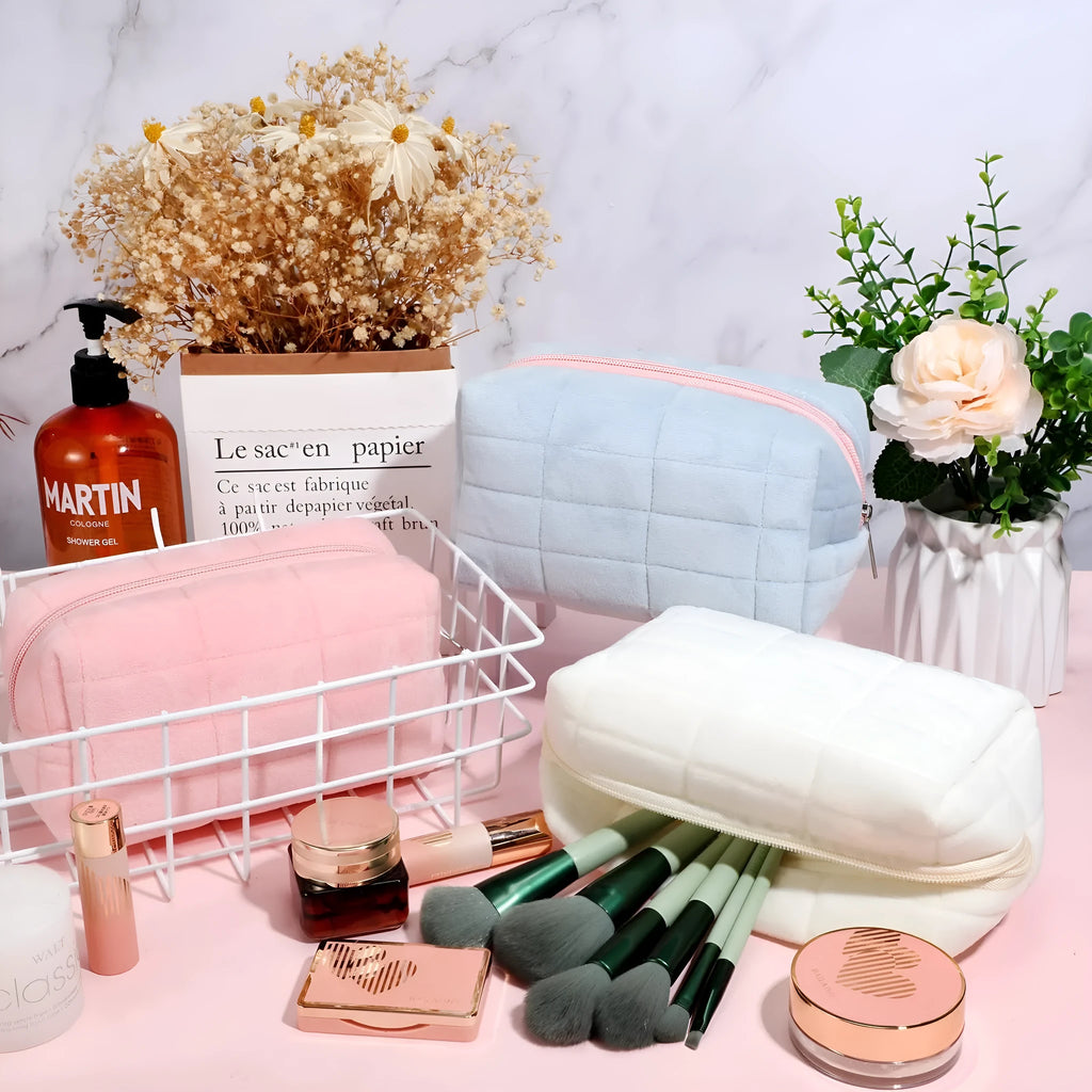 Three plush makeup bags in pink, white, and blue with zippers, laid flat showing front