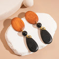 Pair of brown and black wooden retro earrings with an elliptical shape and silver needle detail.