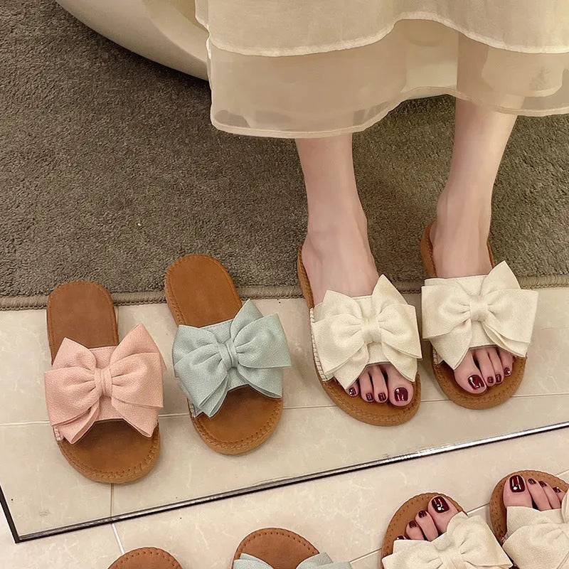 Women's beige suede slip-on sandals with a bow detail and soft rubber sole.