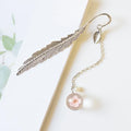 Close-up of a metal alloy bookmark with a preserved pink dried flower inside, measuring 12cm long, on an open book.