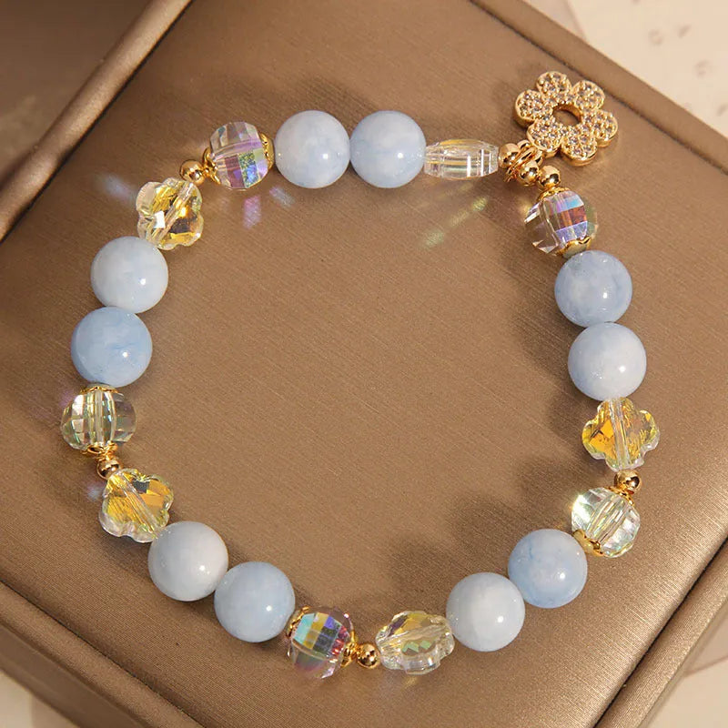Women's aquamarine crystal bracelet with a four-leaf clover charm and pearl accent on wrist.