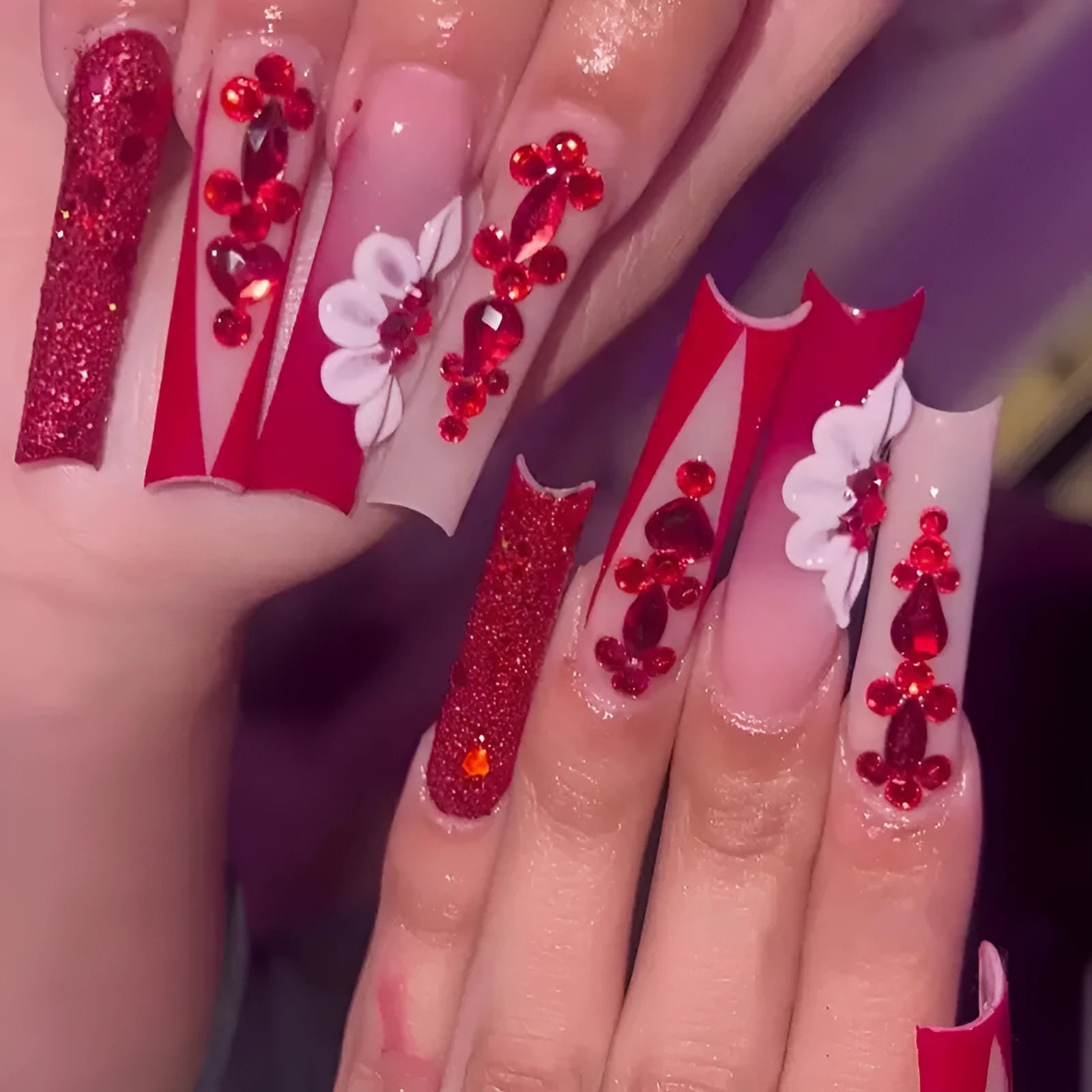 Long almond-shaped false nails with red diamond and floral art in sweet style.
