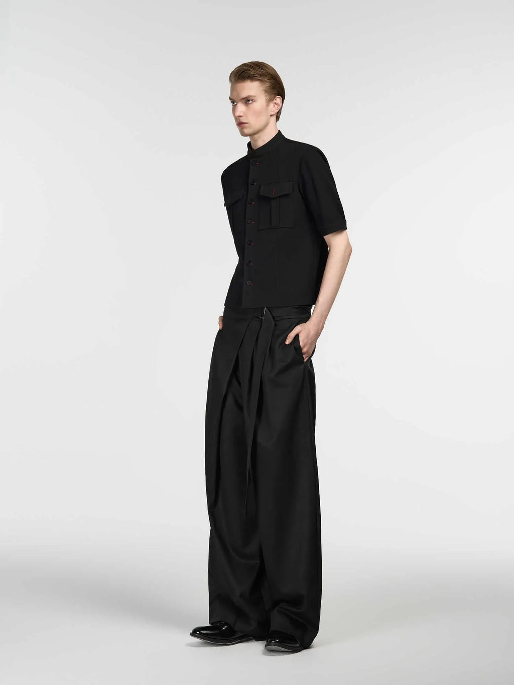 Black straight-leg trousers with adjustable waist and single pleat detail on a hanger.